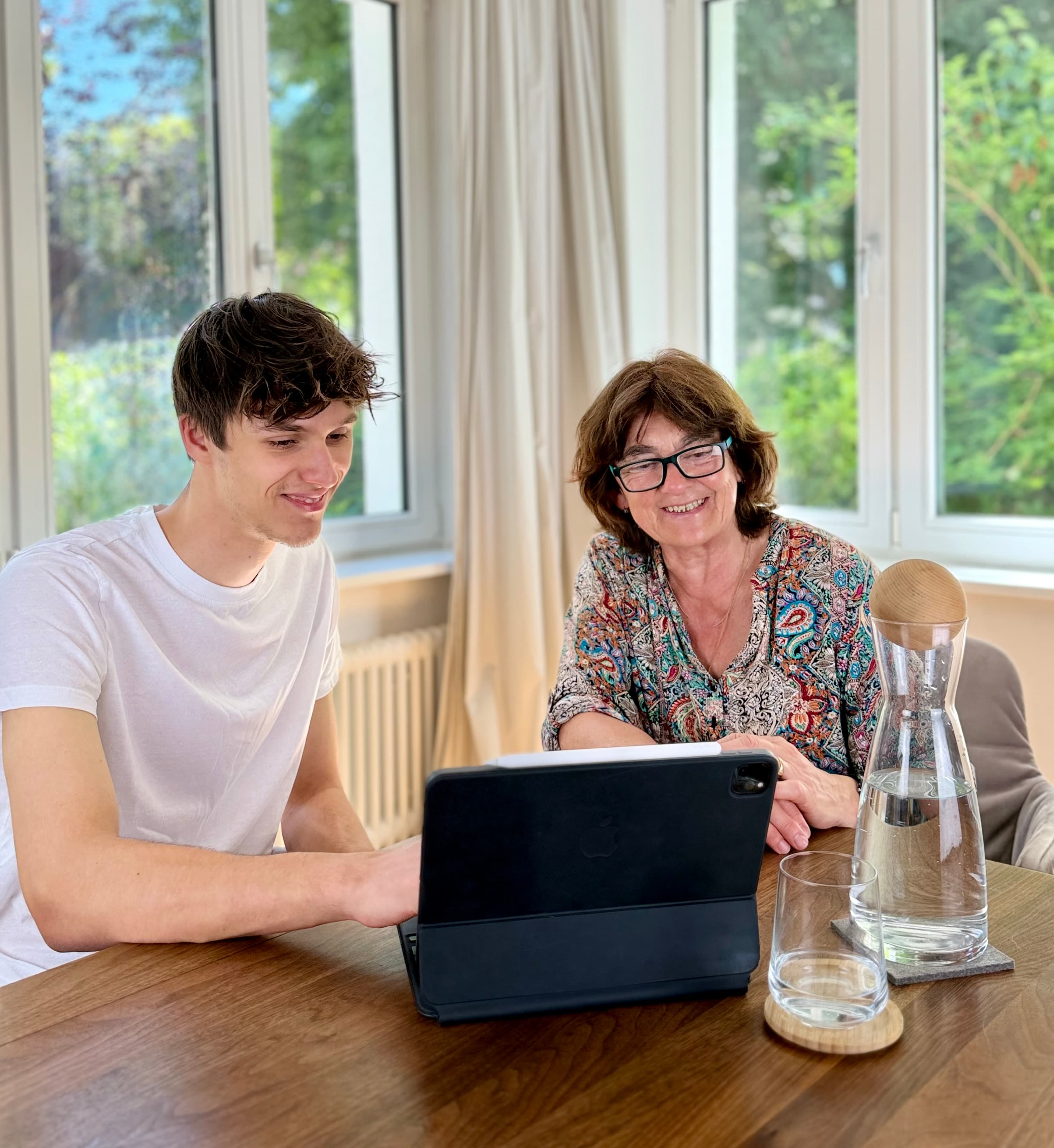 Sebastian zeigt Lena am Esszimmertisch etwas Digitales am Laptop.